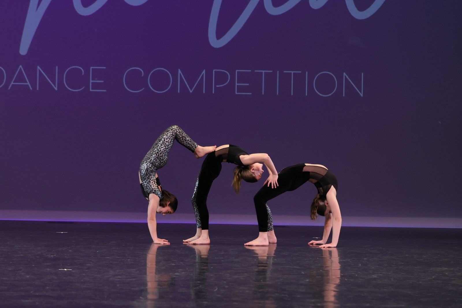 Three Phoenix dancers in a synchronised backbend on a competition stage